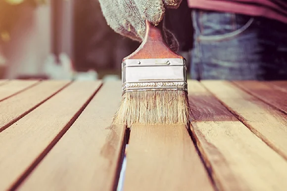 Person streicht Holzlatten mit Pinsel